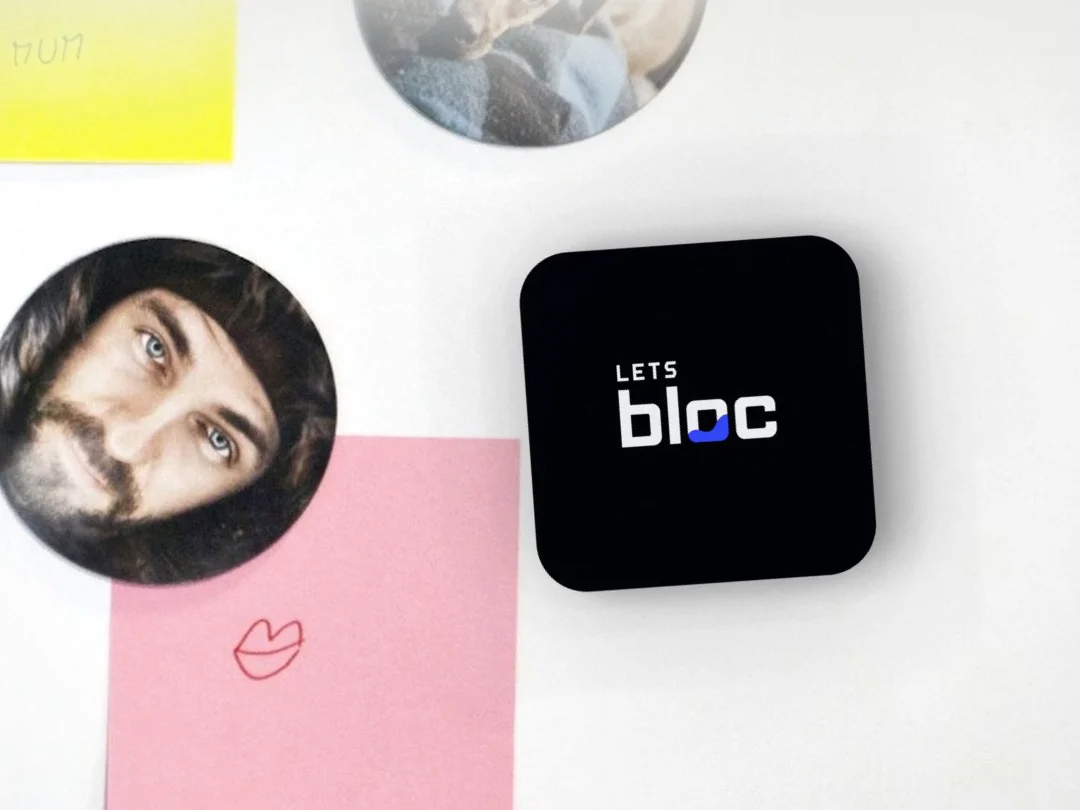 A black bloc on a fridge door, between a sticky note and a photo magnet