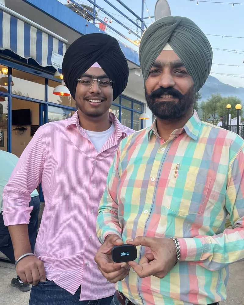 Two smiling bloc owners at a hillside cafe at dusk, the older one holding his bloc toward the camera