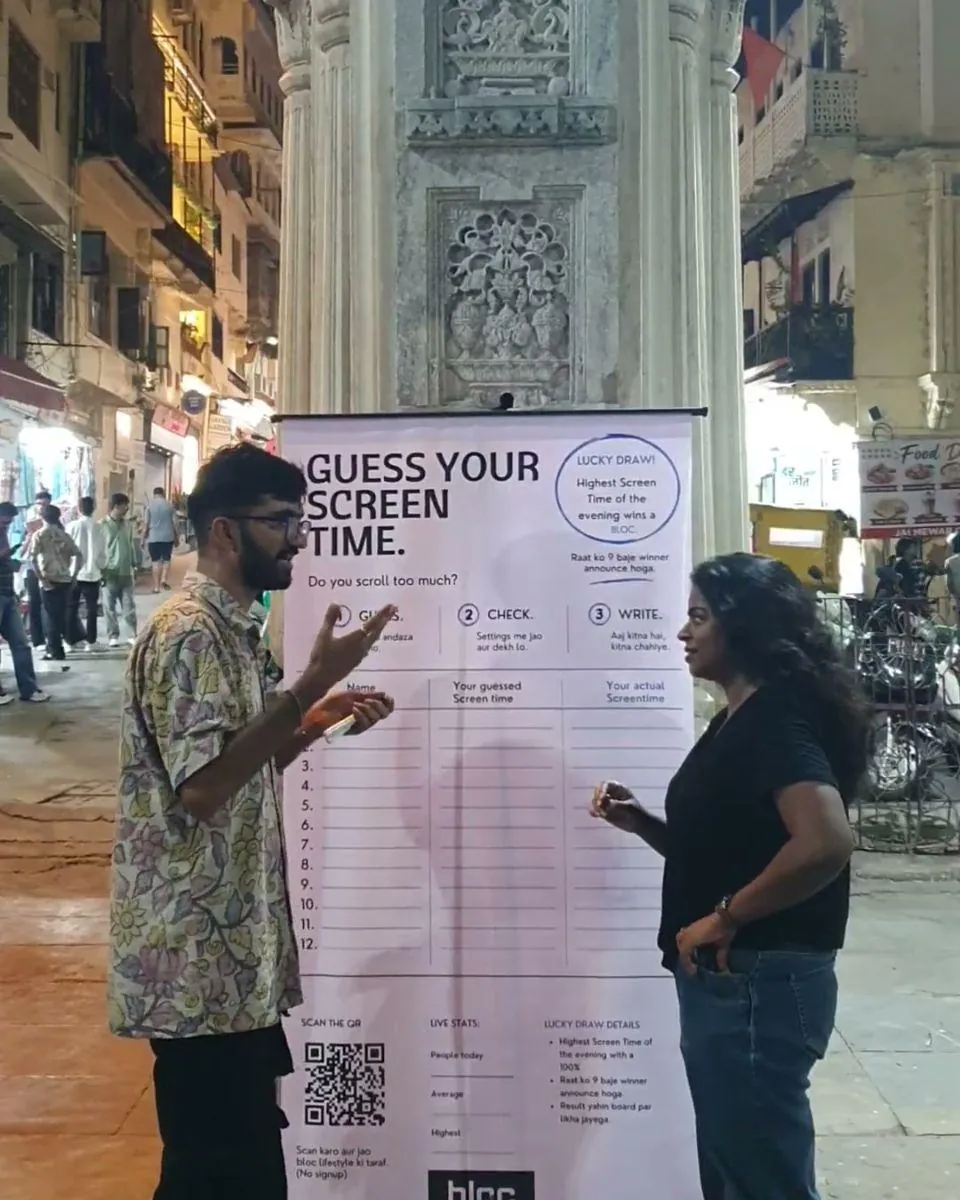 At the Guess your screen time board under the carved gate of Gangaur Ghat at night, talking to a woman holding her phone
